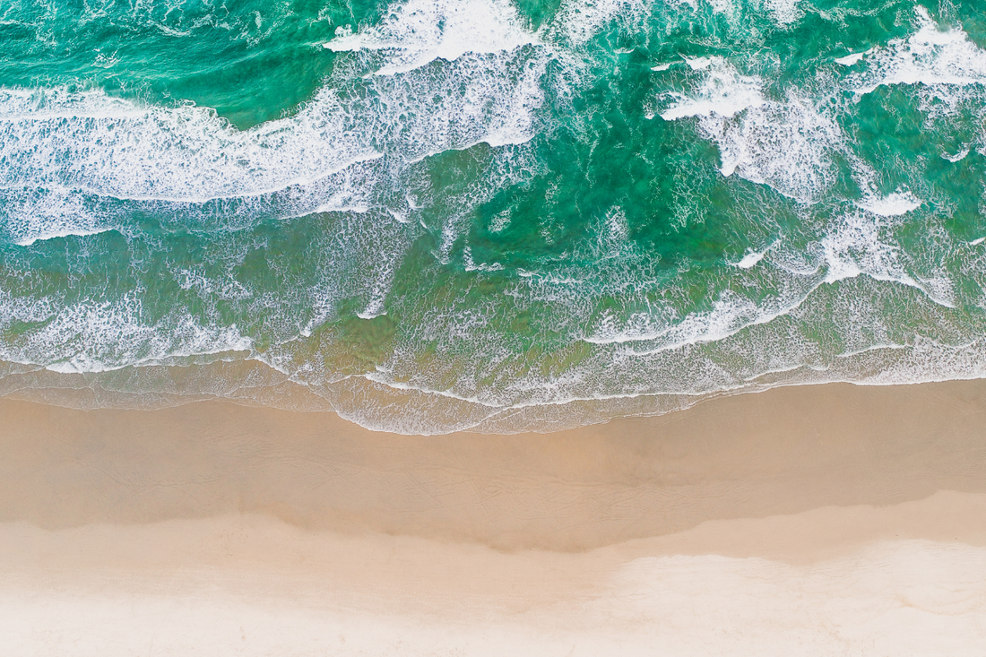 An image of teal and blue waves crashing onto tan and camel-colored sand.