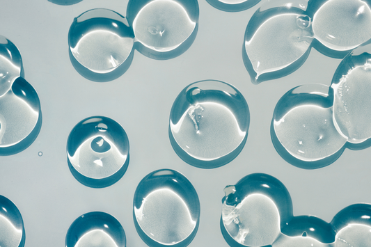 Circular droplets of a clear, viscuous substance resembling hyaluronic acid are set against a blue background.