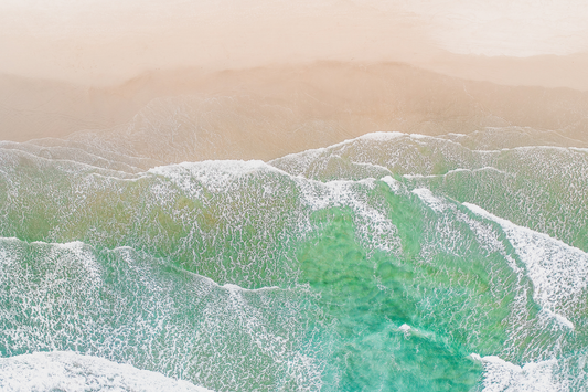 Green and blue waves crash onto beige sand.